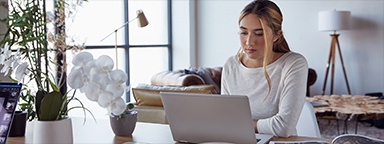 Gadis duduk dan bekerja pada laptop di meja dalam rumahnya