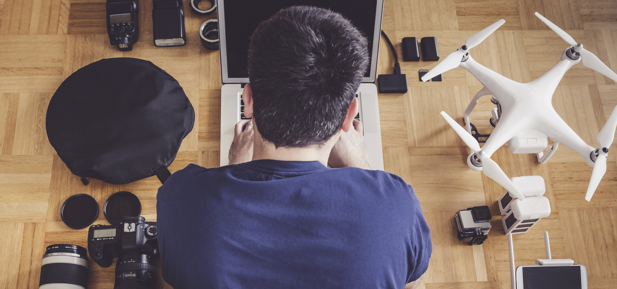 A man using a laptop in the floor with a drone, DSLR, and action cam nearby